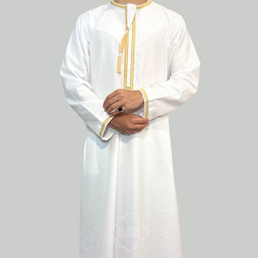 Model wearing a White collarless omani thobe with sophisticated gold embroidery on a plain background.