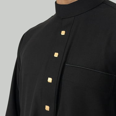 Black collared thobe close up with gold buttons on a gray background