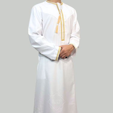 Model wearing a White collarless omani thobe with sophisticated gold embroidery on a plain background.